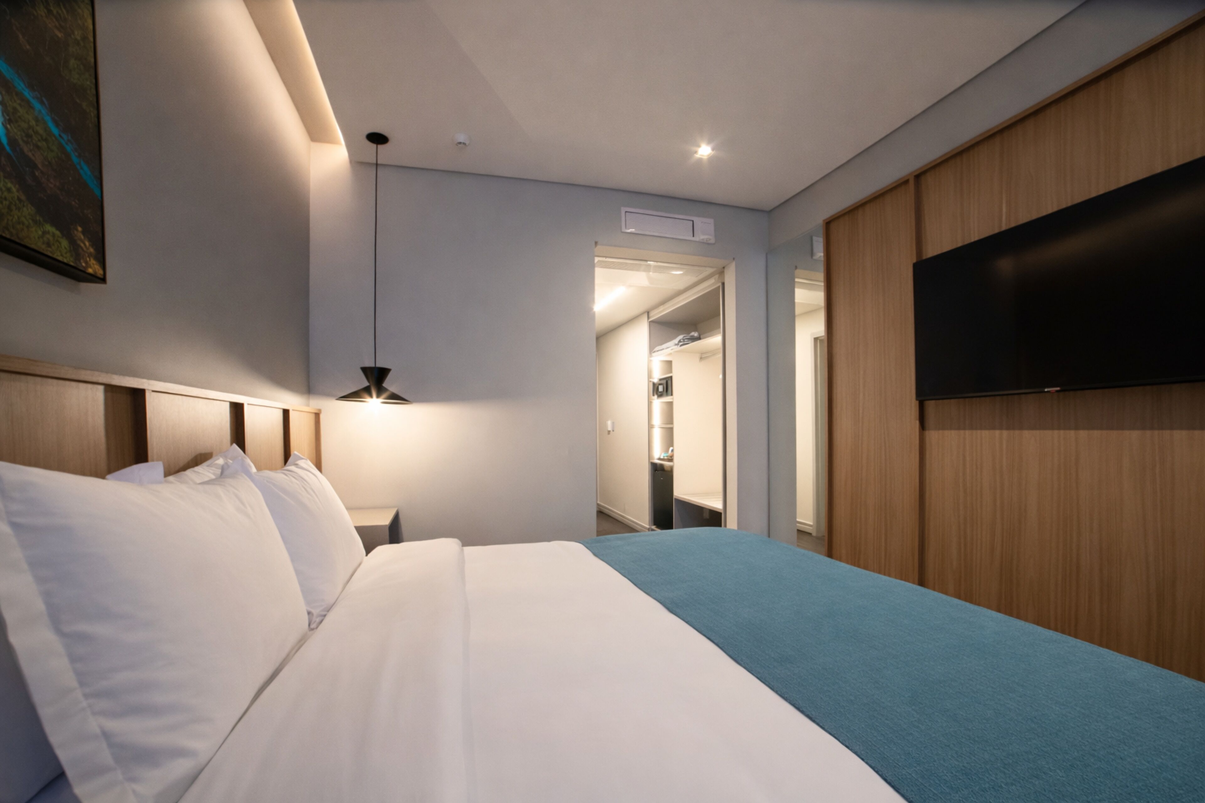 Habitación de hotel con cama, televisión montada en la pared, lámpara de techo y puerta que da a un baño.