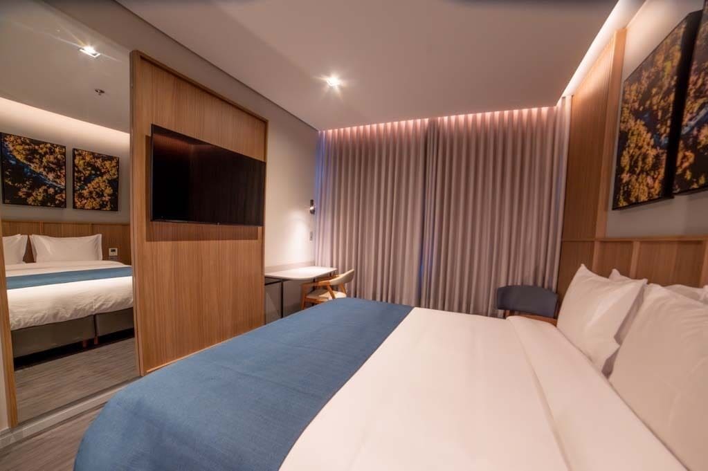 A hotel room with a large bed, a desk, a chair, and a TV.