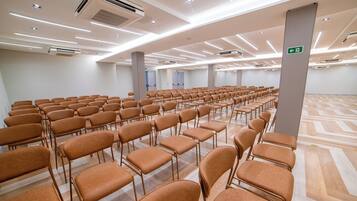 A large conference room with rows of chairs, air conditioning units, and a patterned floor.