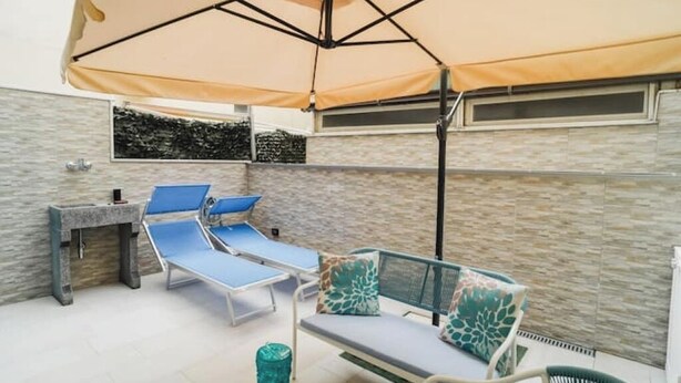 A sunlit outdoor seating area with a table and chairs, a stone wall, and a large umbrella providing shade. - Euterpe Apartment - Harmony, Relaxation and Sea at the Abode of the Muses (Praia a Mare)