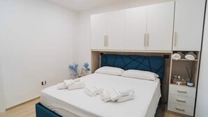 A neatly arranged bedroom with a bed, white cabinets, and a small bedside table with a decorative item. - Euterpe Apartment - Harmony, Relaxation and Sea at the Abode of the Muses (Praia a Mare)