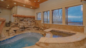 A spa area with a stone wall, a hot tub, and large windows offering a view. - Mountain Cascades: Pool*Views*Theater*Games*Wifi*HotTub*Luxury (Sevierville)