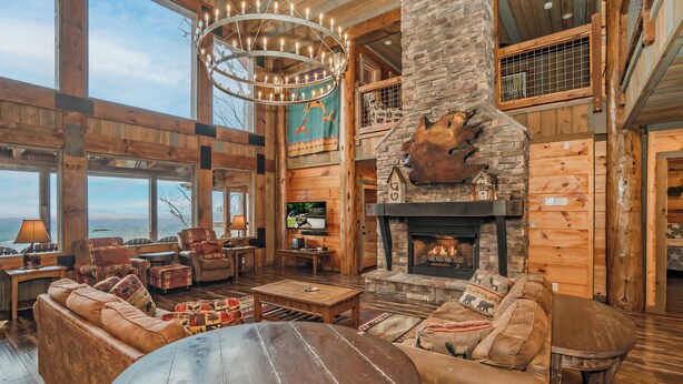 A spacious living room with a stone fireplace, leather sofas, and a large wooden table. - Mountain Cascades: Pool*Views*Theater*Games*Wifi*HotTub*Luxury (Sevierville)