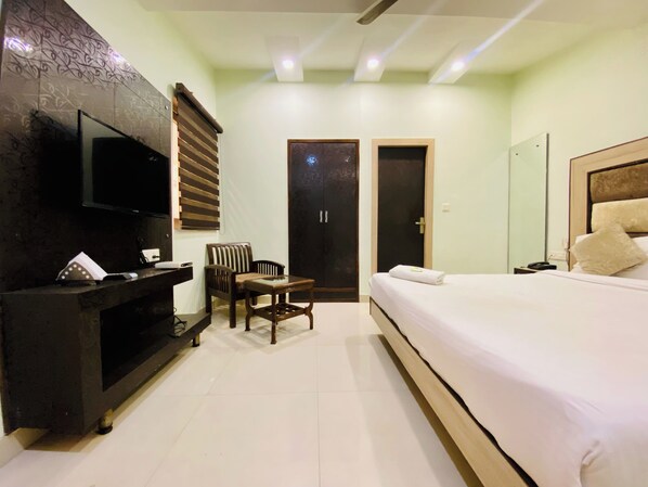 Una habitación de hotel con cama, televisor montado en la pared, escritorio y silla, además de una puerta.