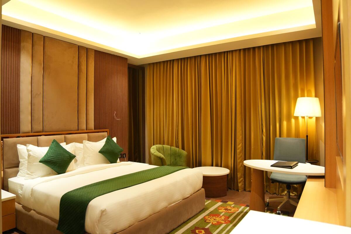A hotel room with a bed, a desk, a chair, and a lamp.