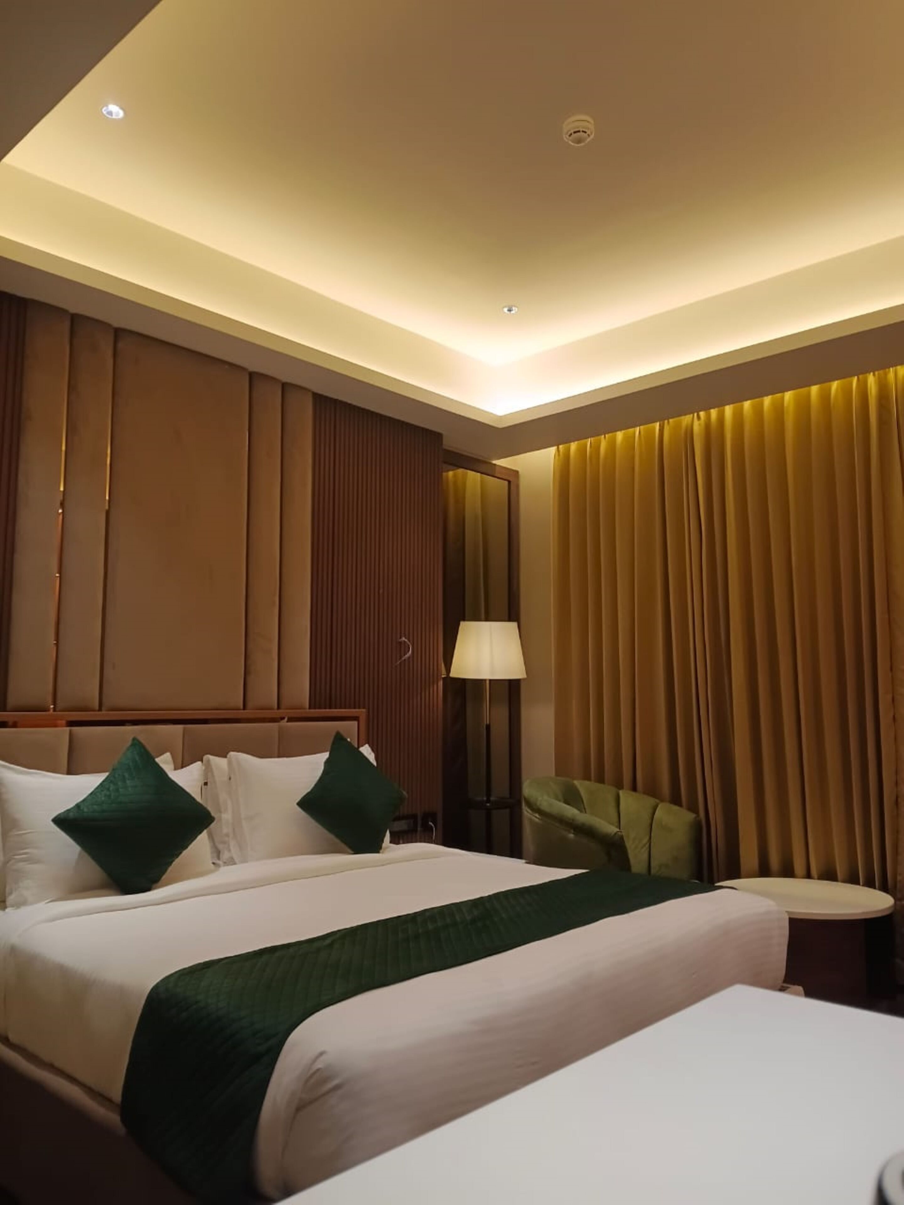A hotel room with a large bed, a bedside table, a lamp, and a chair.