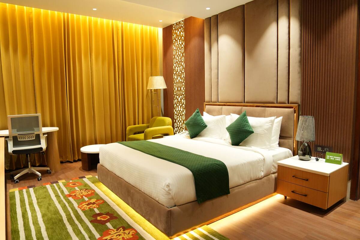 A hotel room with a bed, bedside table, lamp, and a desk with a chair.