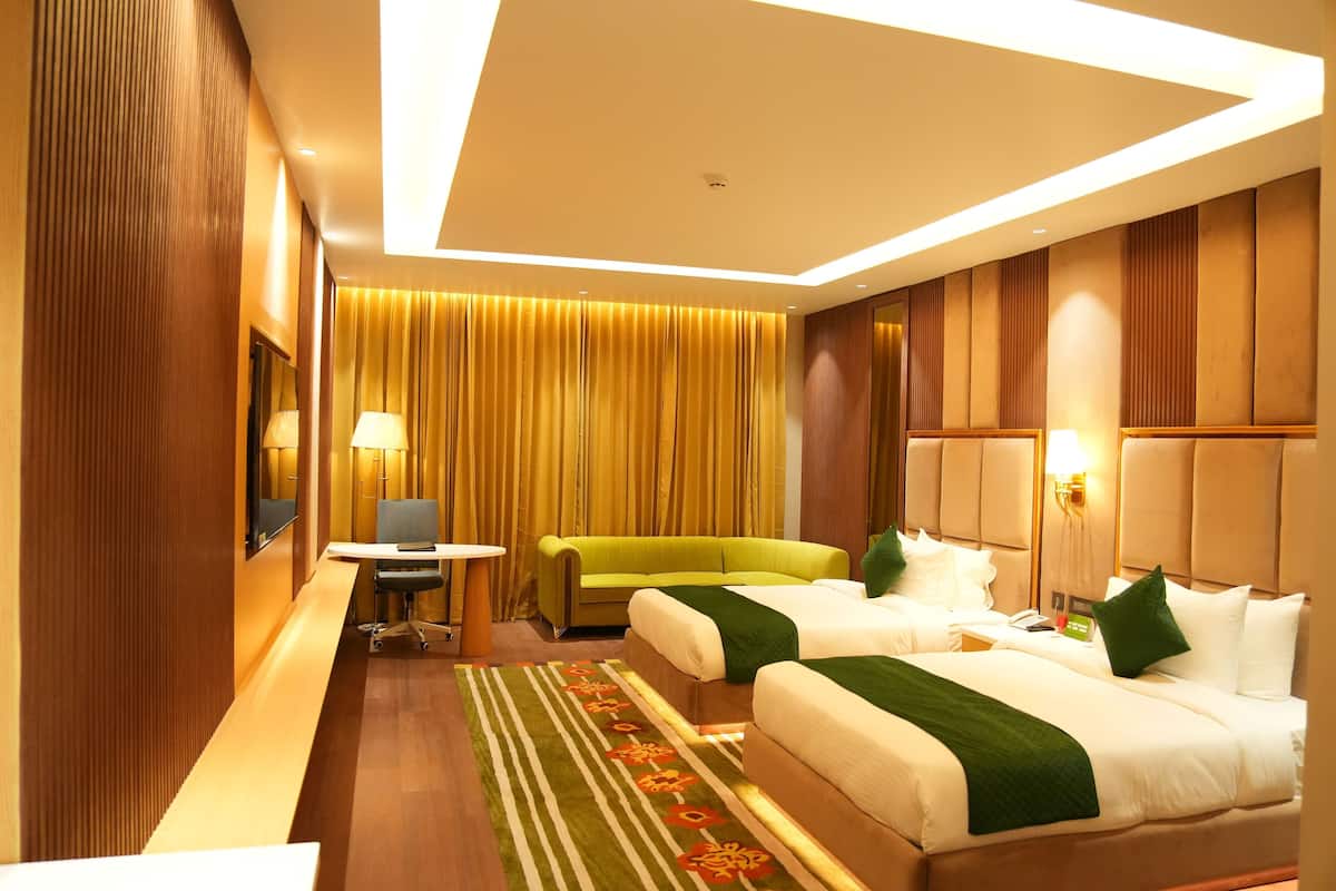 A hotel room with two beds, a desk, a chair, and a sofa.