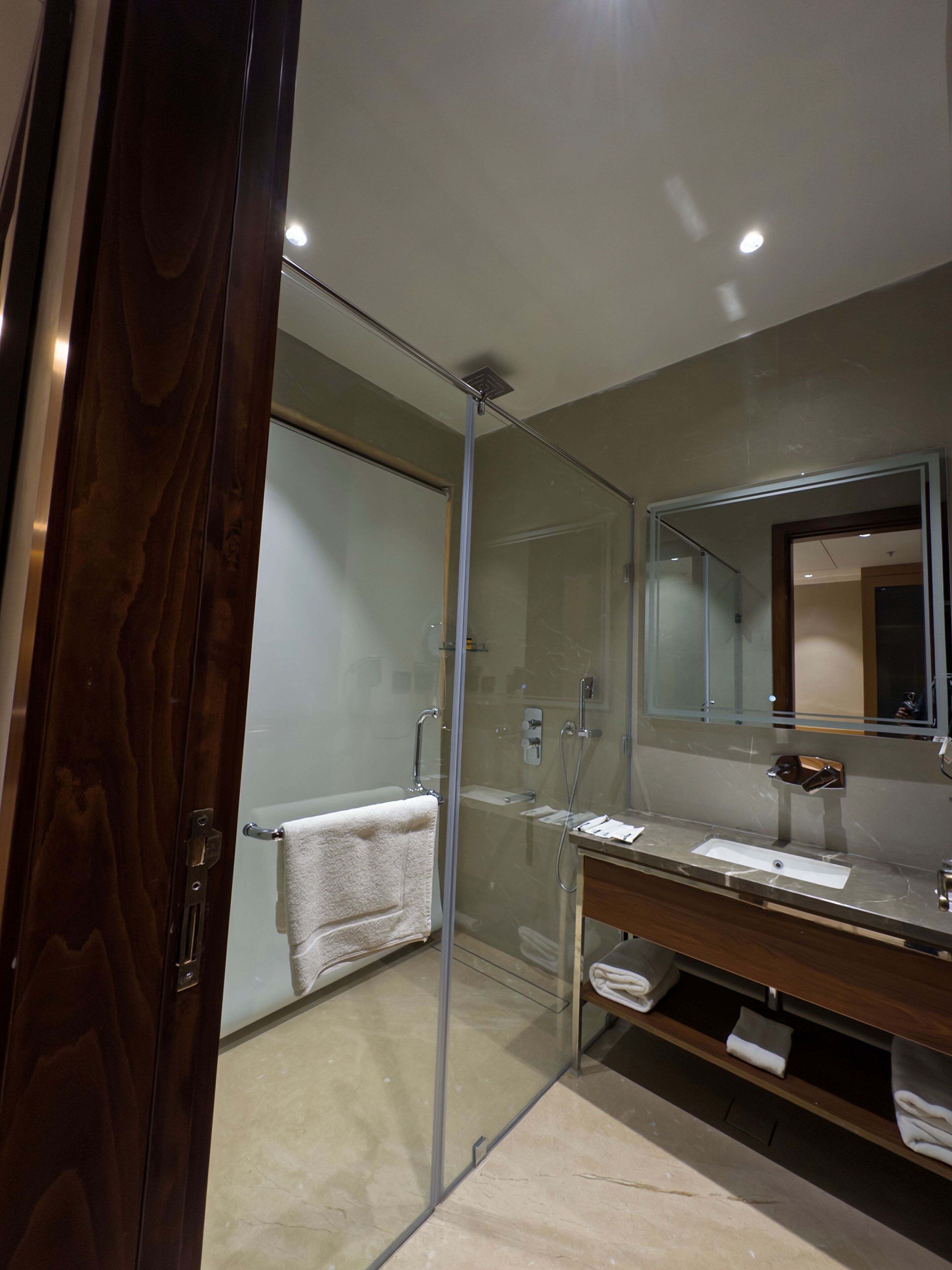Un baño moderno con cabina de ducha de vidrio, tocador con espejo y toallero.