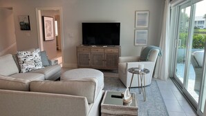 Una sala de estar moderna con un sofá, una mesa de centro, un televisor y vistas al exterior.