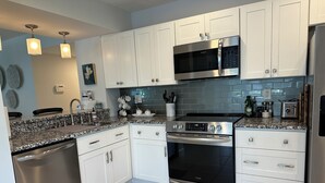 Una cocina moderna con armarios blancos, electrodomésticos de acero inoxidable, encimera de granito y salpicadero.
