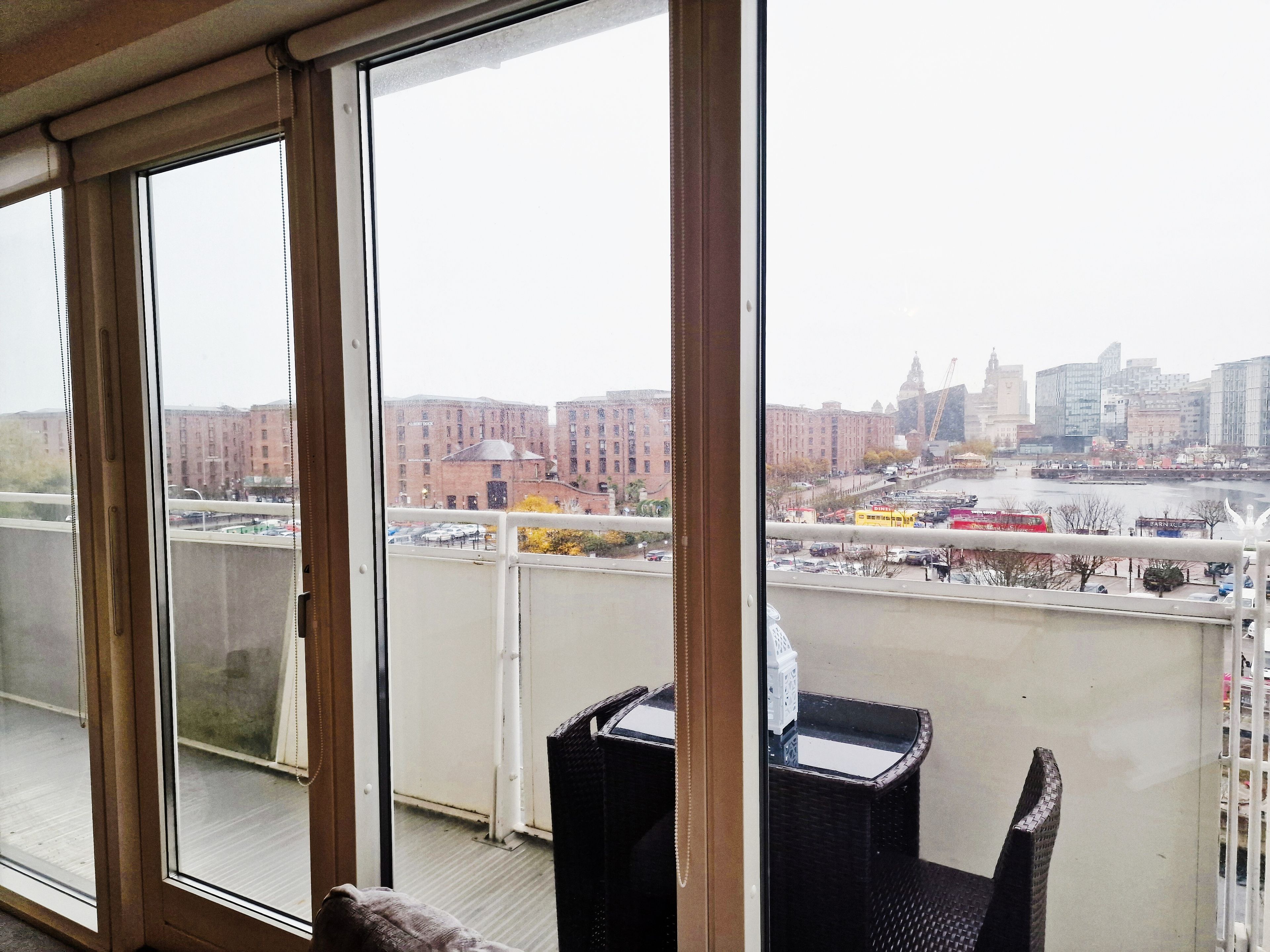 Ein Zimmer mit großen Fenstern und Blick auf eine Stadtlandschaft, darunter ein Fluss und Gebäude.