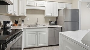 Una cucina moderna con mobili bianchi, elettrodomestici in acciaio inossidabile, lavastoviglie e forno a microonde.