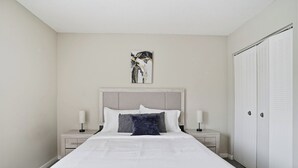 Ett välordnat hotellrum med en stor säng, två sängbord med lampor, en sänggavel, en garderob och ett enda konstverk på väggen.