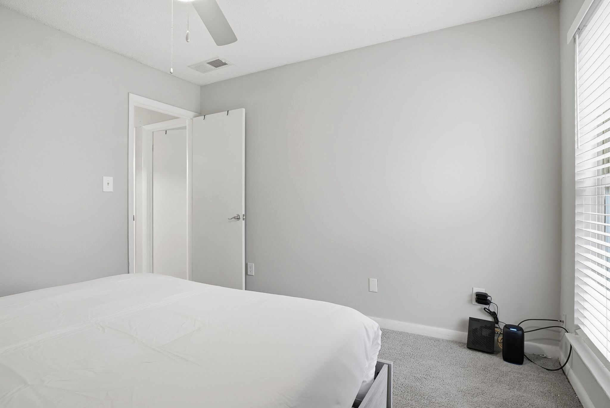 Quarto com cama, porta, janela com persianas e tomada com dispositivo de carregamento.