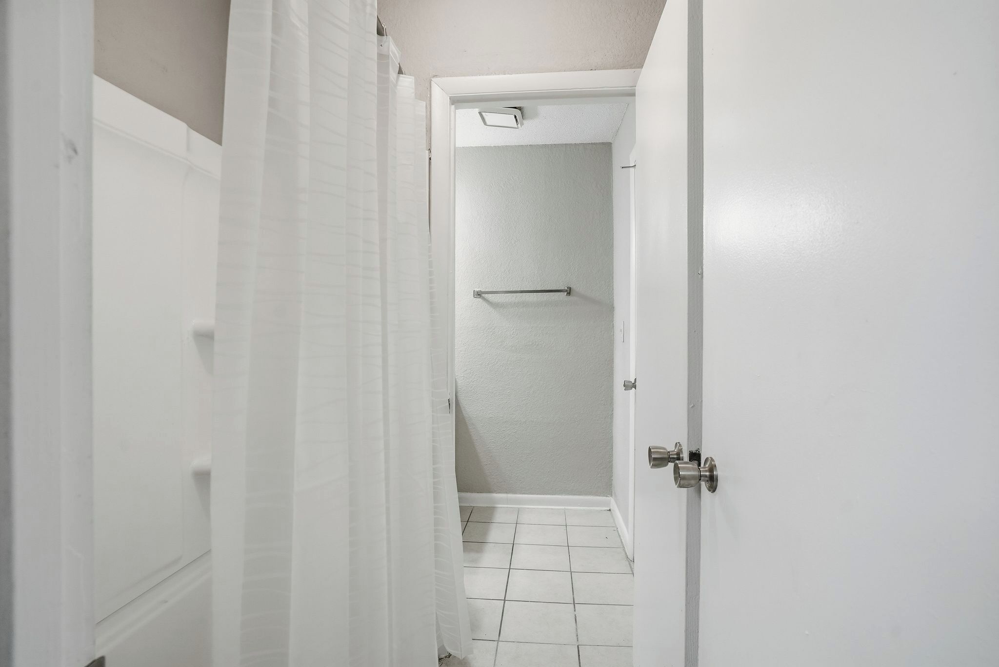 Un corridoio stretto con una porta bianca che dà su un bagno con doccia e porta asciugamani.