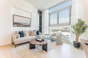 Een moderne woonkamer met een bank, salontafel, stoel, groot raam en een potplant.
