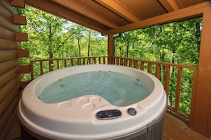 Ein Whirlpool auf einer Holzterrasse mit Blick auf einen Wald.