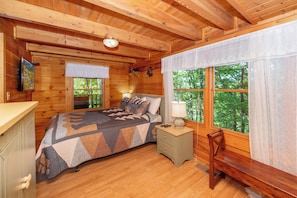 Ein Schlafzimmer einer Holzhütte mit Bett, Nachttisch, Bank und Fernseher an der Wand.