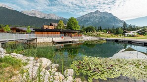 A lakeside hotel with a wooden deck, a pond with lily pads, and mountains in the background. - Hotel Gerhardhof by ami (Wildermieming)