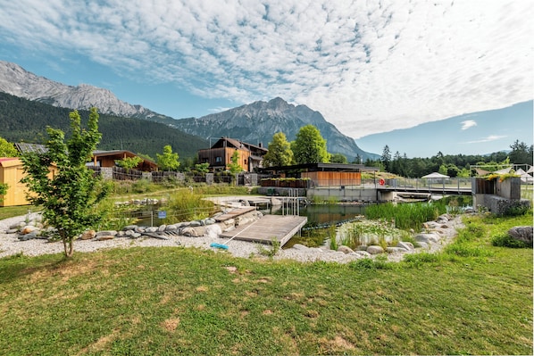 Una baita sul lago con veranda in legno, un piccolo molo e montagne sullo sfondo.