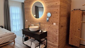A modern bathroom with a wooden vanity, a round mirror, and a built-in sink. - Hotel Gerhardhof by ami (Wildermieming)