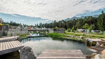 Un muelle de madera que se adentra en un río tranquilo, con un puente al fondo y una cadena montañosa cubierta de bosques.