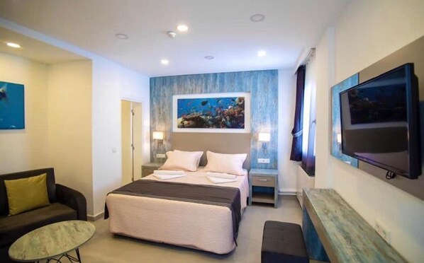A hotel room with a bed, a desk, a TV, a sofa, and a painting on the wall. - Queen Victoria Suit Apart otel (Bodrum)