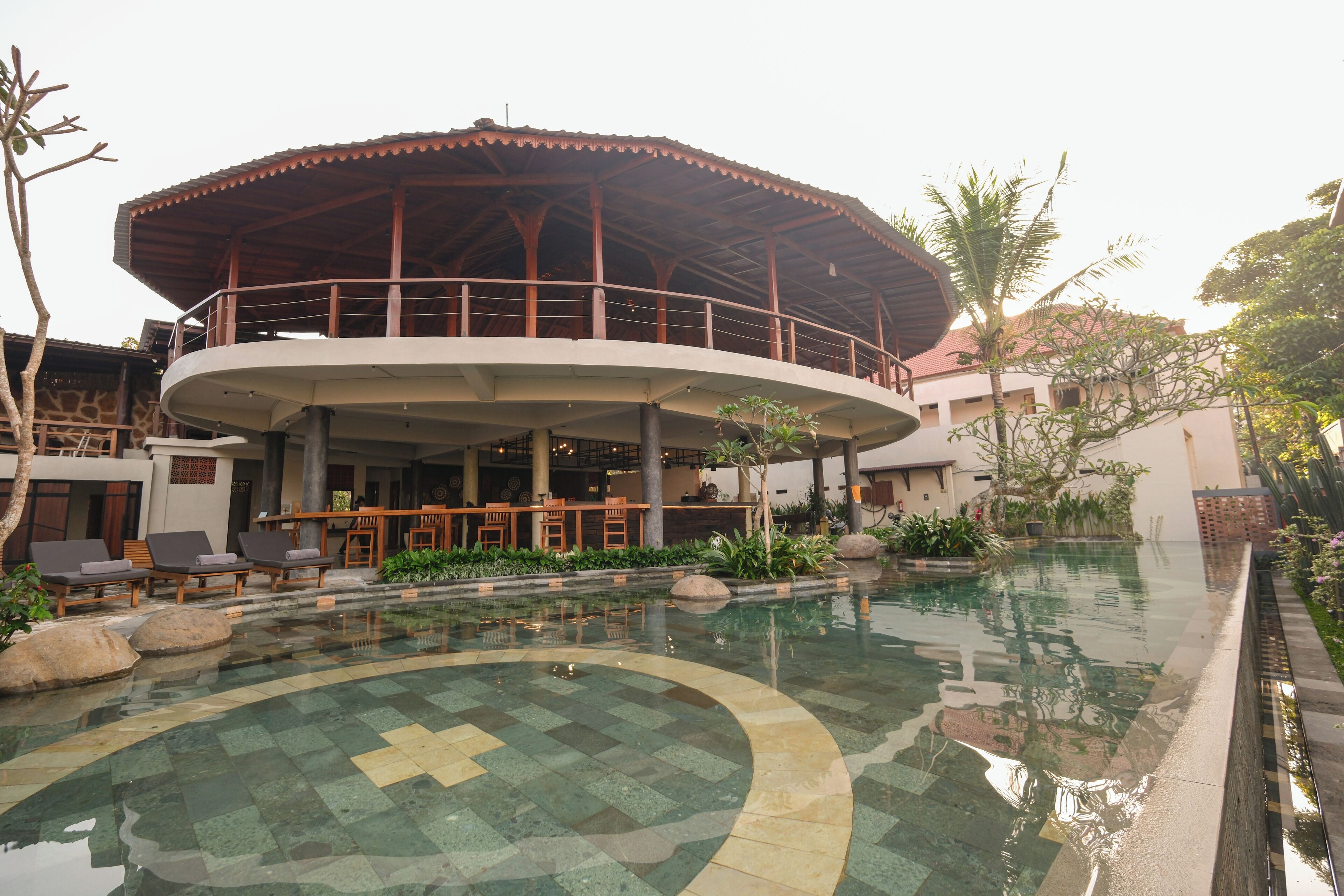 A resort with a circular pool, a covered outdoor seating area, and a building with a distinctive roof.