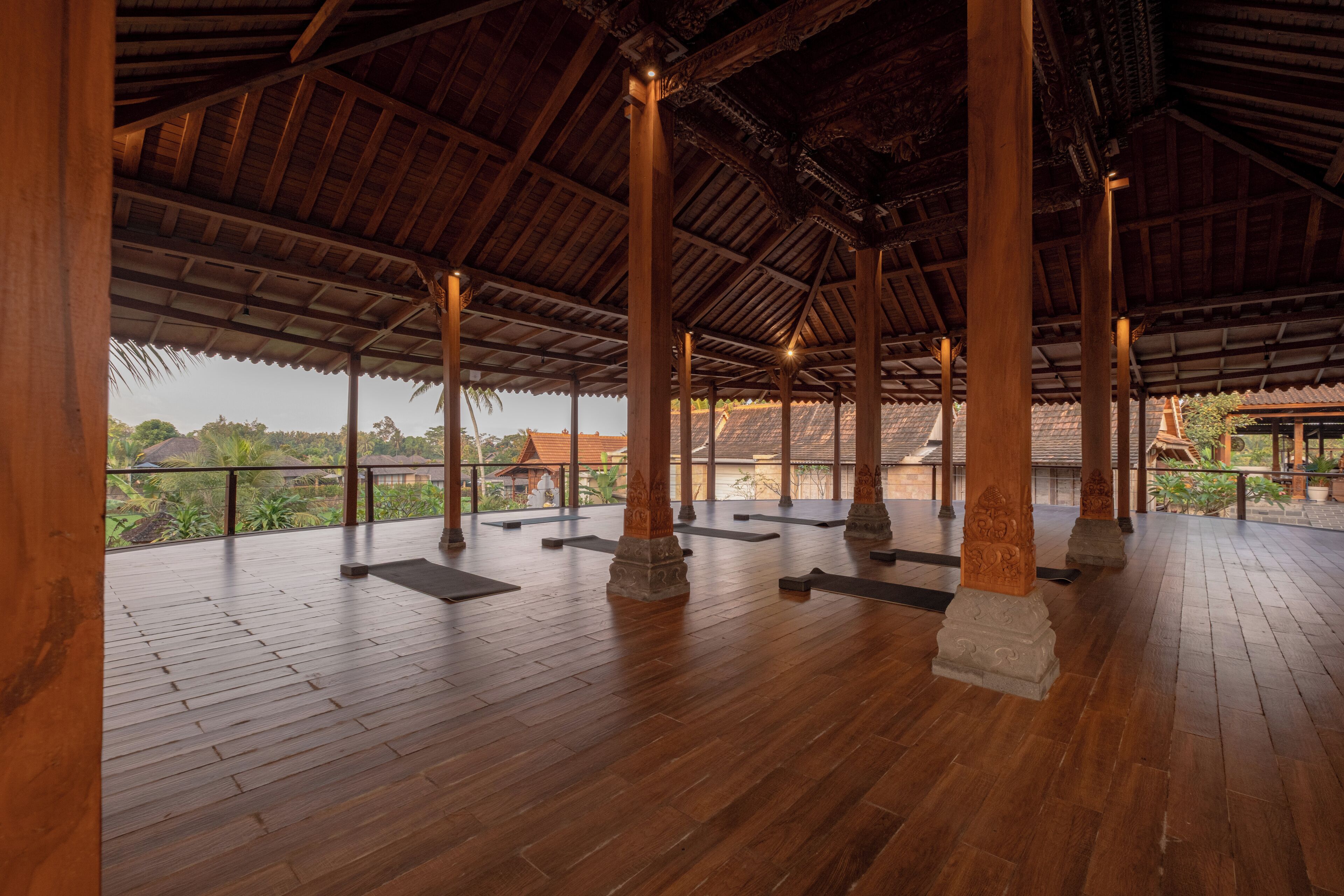 An open pavilion with wooden flooring and columns, featuring a view of distant buildings and greenery.