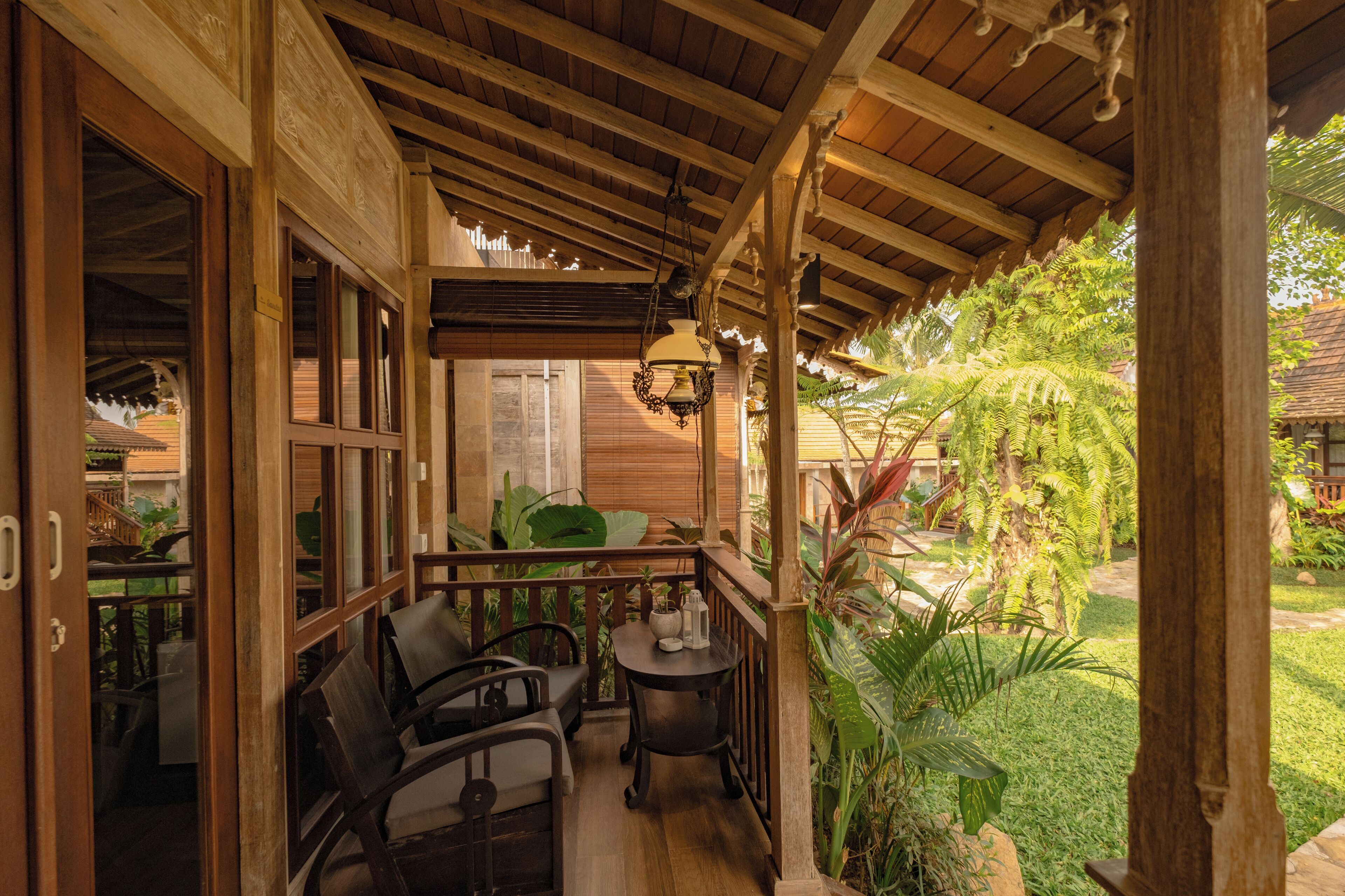 A wooden porch with a table and chairs, surrounded by lush greenery.