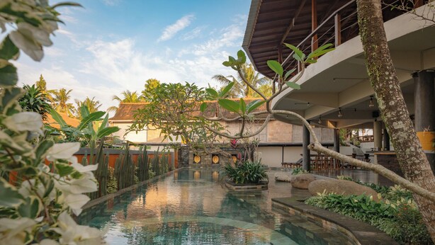 A serene pool area with a curved design, surrounded by lush greenery and a traditional building with a tiled roof. - Artropeace Ubud Retreat & Villas (Ubud)