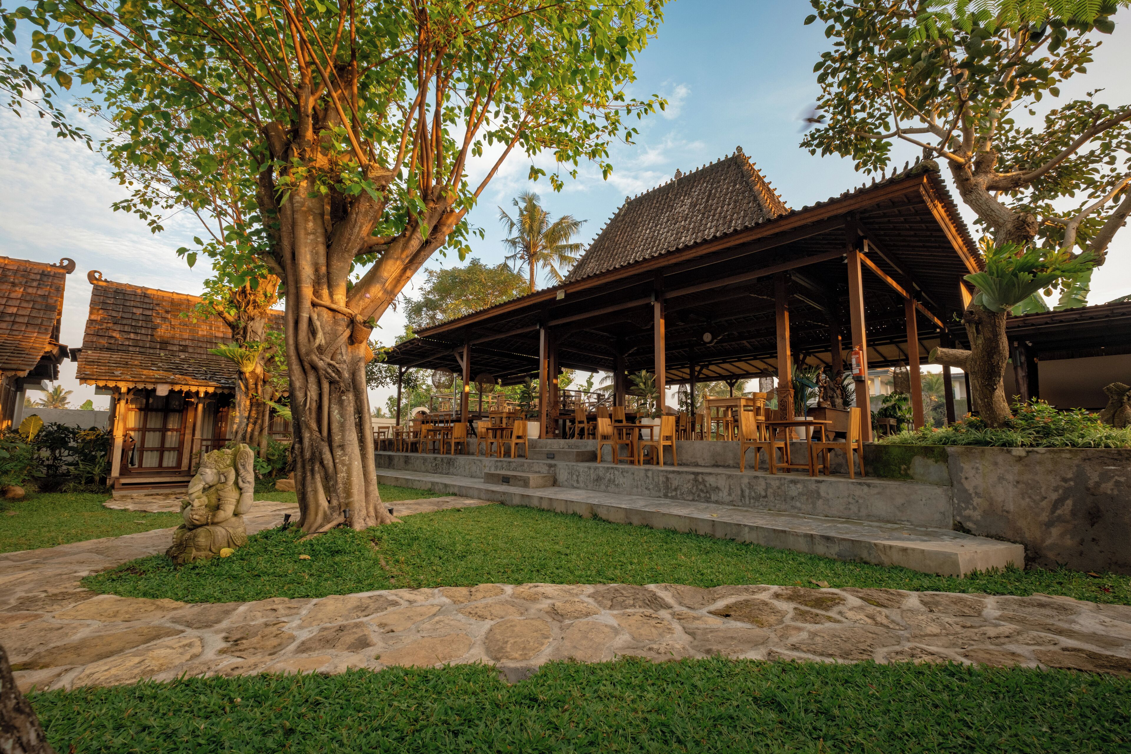 A traditional wooden pavilion with stone steps leading up to it, surrounded by lush greenery and a stone pathway.