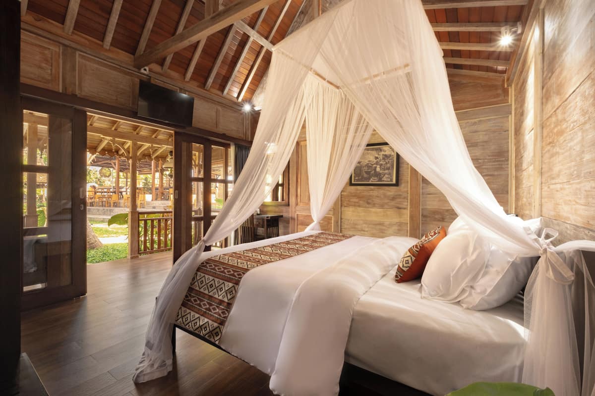 Ein Schlafzimmer mit Baldachinbett, Holzboden und Blick auf einen Außenbereich.