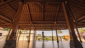 Un pabellón cubierto con techo de madera y columnas, donde una persona realiza una postura de yoga.
