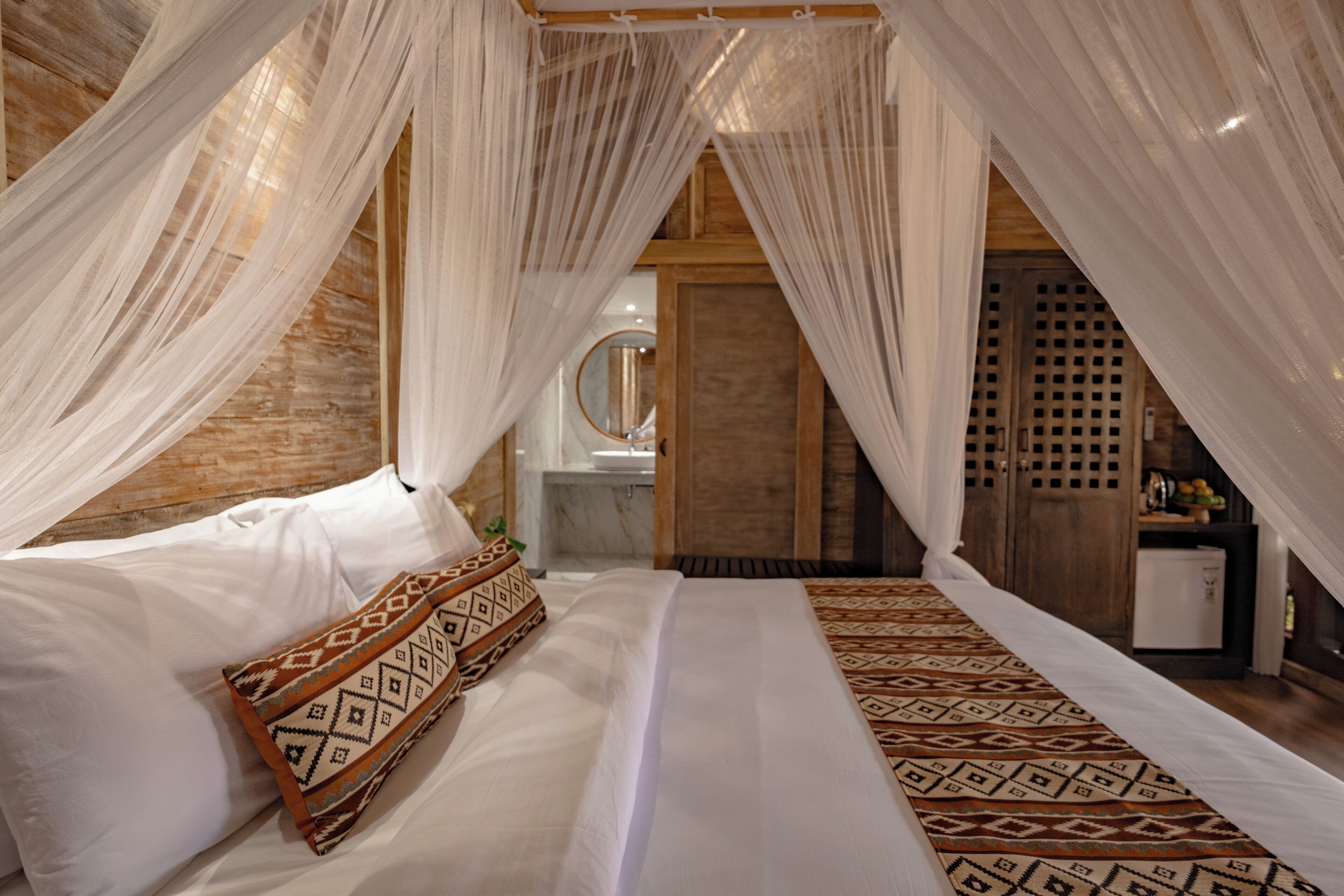 A bedroom with a bed, white bedding, a patterned throw, and sheer curtains.