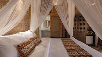 A bedroom with a bed, white bedding, a patterned throw, and sheer curtains.