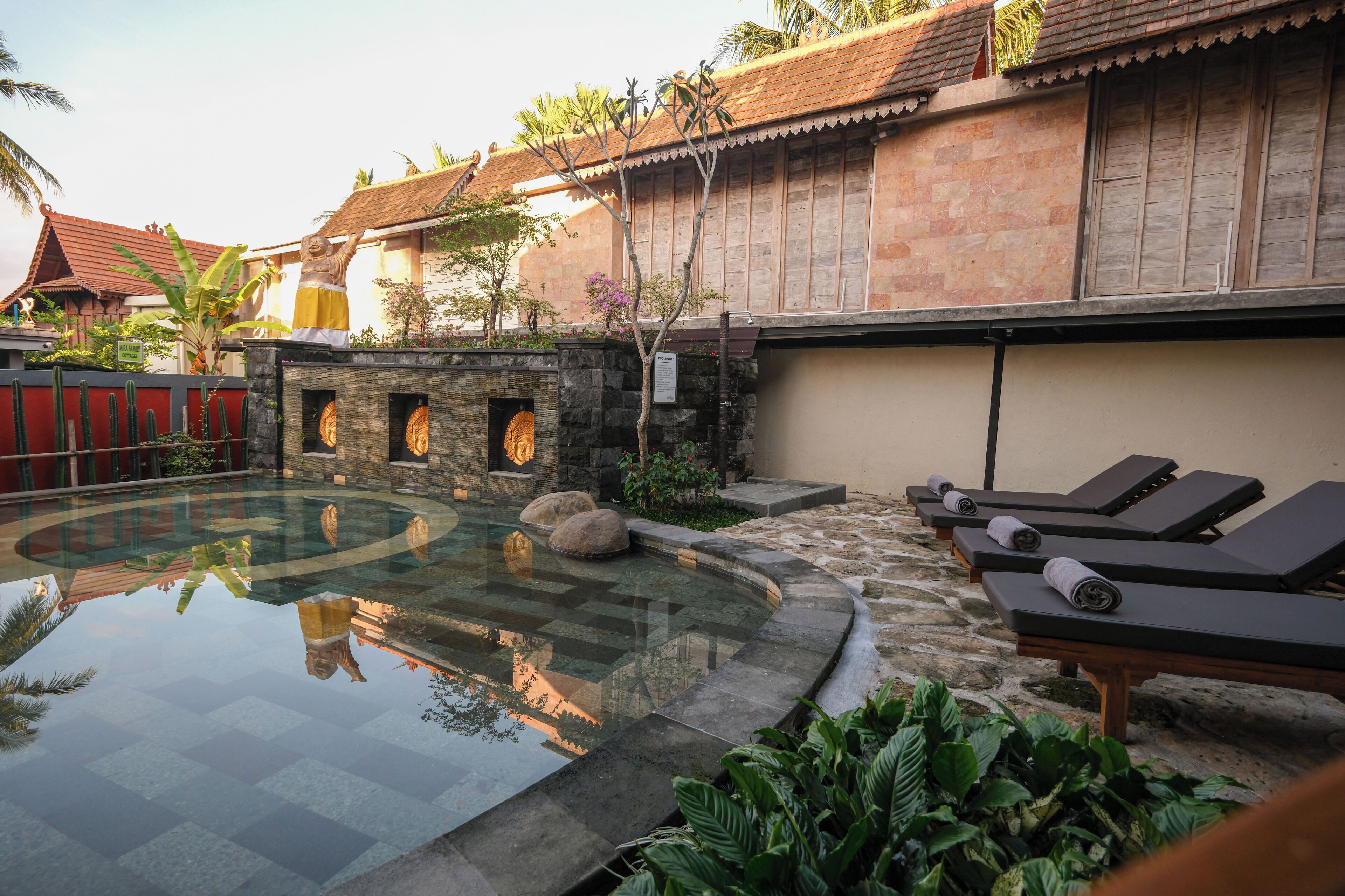 A swimming pool with lounge chairs, a stone wall, and tropical plants.