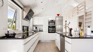 Une cuisine moderne avec des meubles blancs, un plan de travail noir, des appareils électroménagers en acier inoxydable et une fenêtre qui laisse entrer la lumière naturelle.