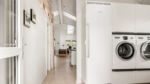 Une buanderie équipée de machines à laver Bosch, d’un banc en bois et donnant sur la cuisine.