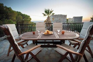 A round wooden table with four chairs, a plate of food, and two glasses of water. - Kitta Mani Towerhouse - Mountain Views Garden (East Mani)