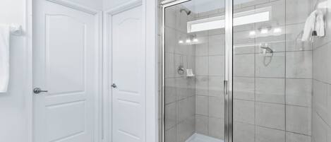 Une salle de bain moderne avec une douche à parois de verre, des murs recouverts de carreaux blancs et une porte sur laquelle est accrochée une serviette.