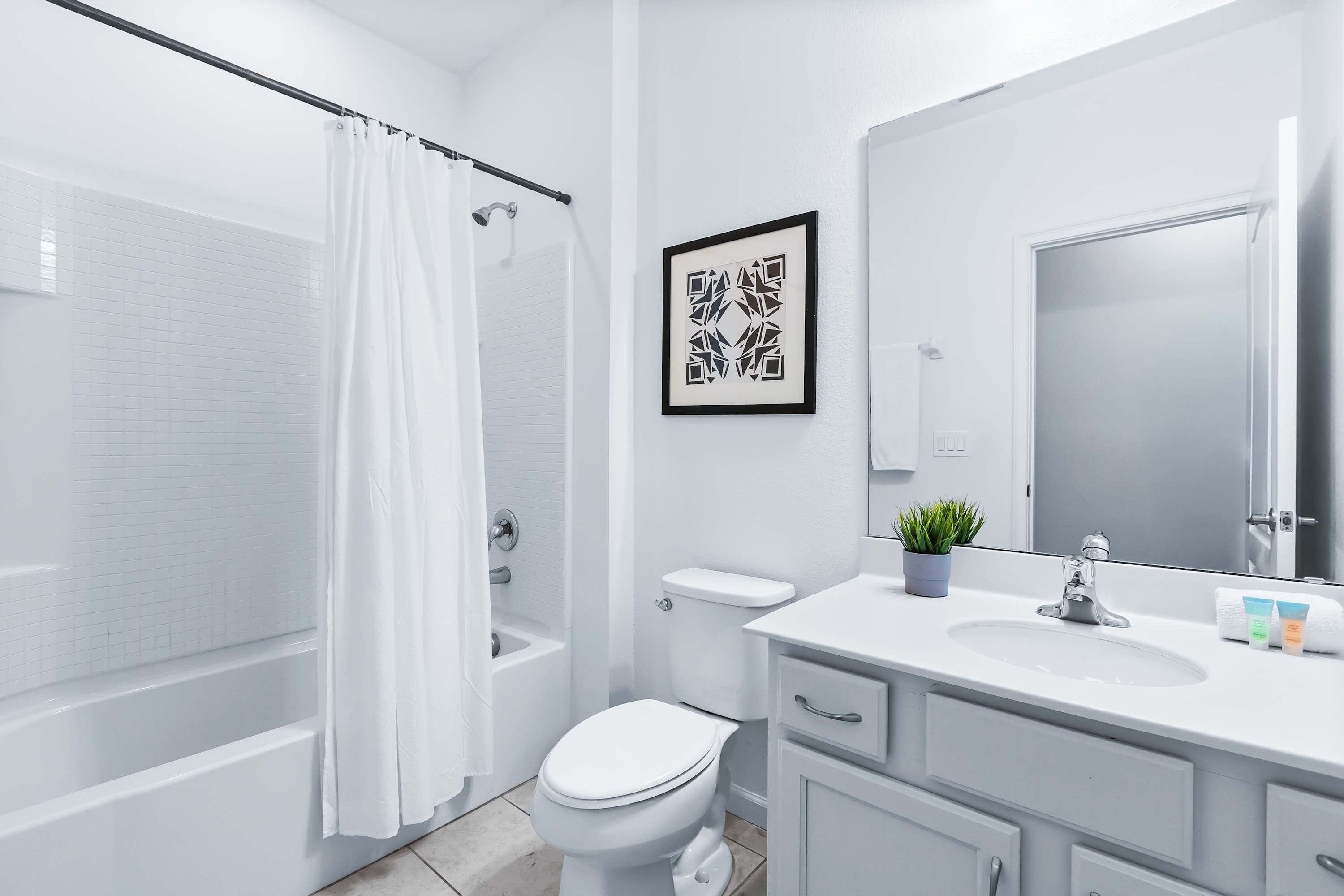 A modern bathroom with a bathtub, toilet, sink, and a framed artwork on the wall.