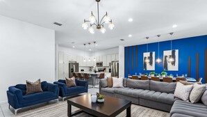 Un salon moderne comprenant un canapé, deux fauteuils, une table basse et un coin repas avec une cuisine en arrière-plan.