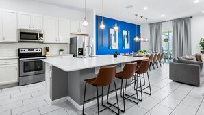 Une cuisine moderne avec des meubles blancs, des appareils en acier inoxydable et un îlot central doté de tabourets de bar.