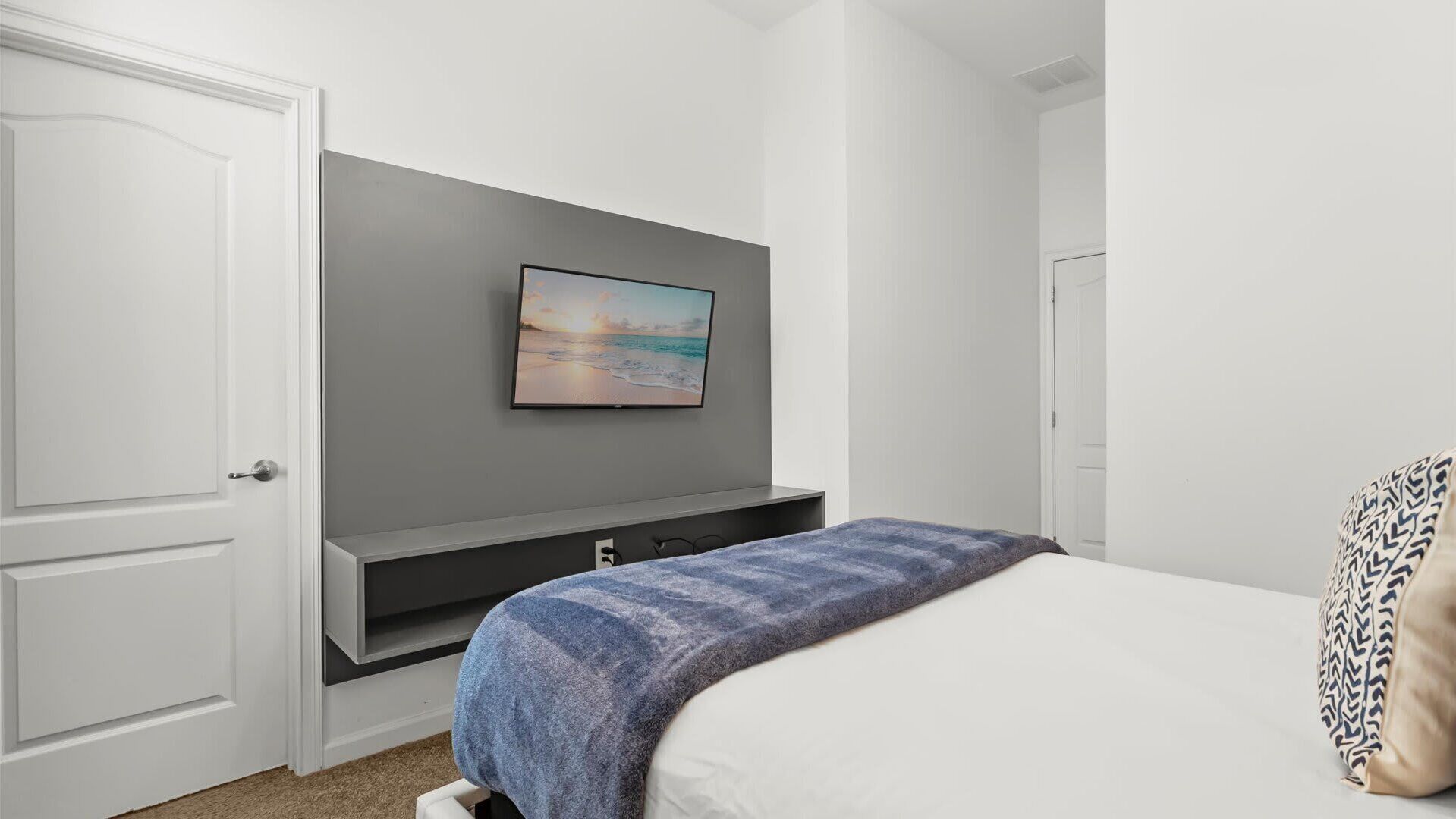A bedroom with a bed, a TV mounted on the wall, and a door.