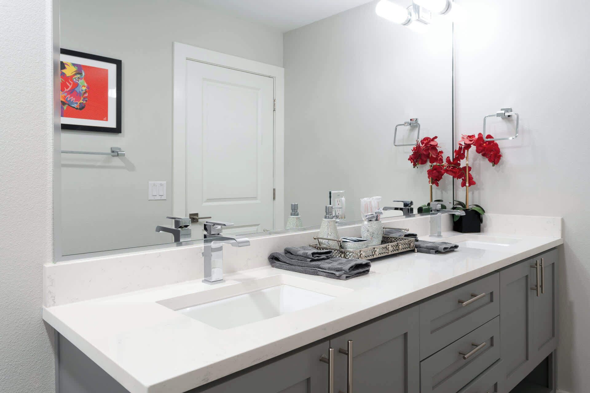 A modern bathroom with two sinks, a large mirror, and a door.