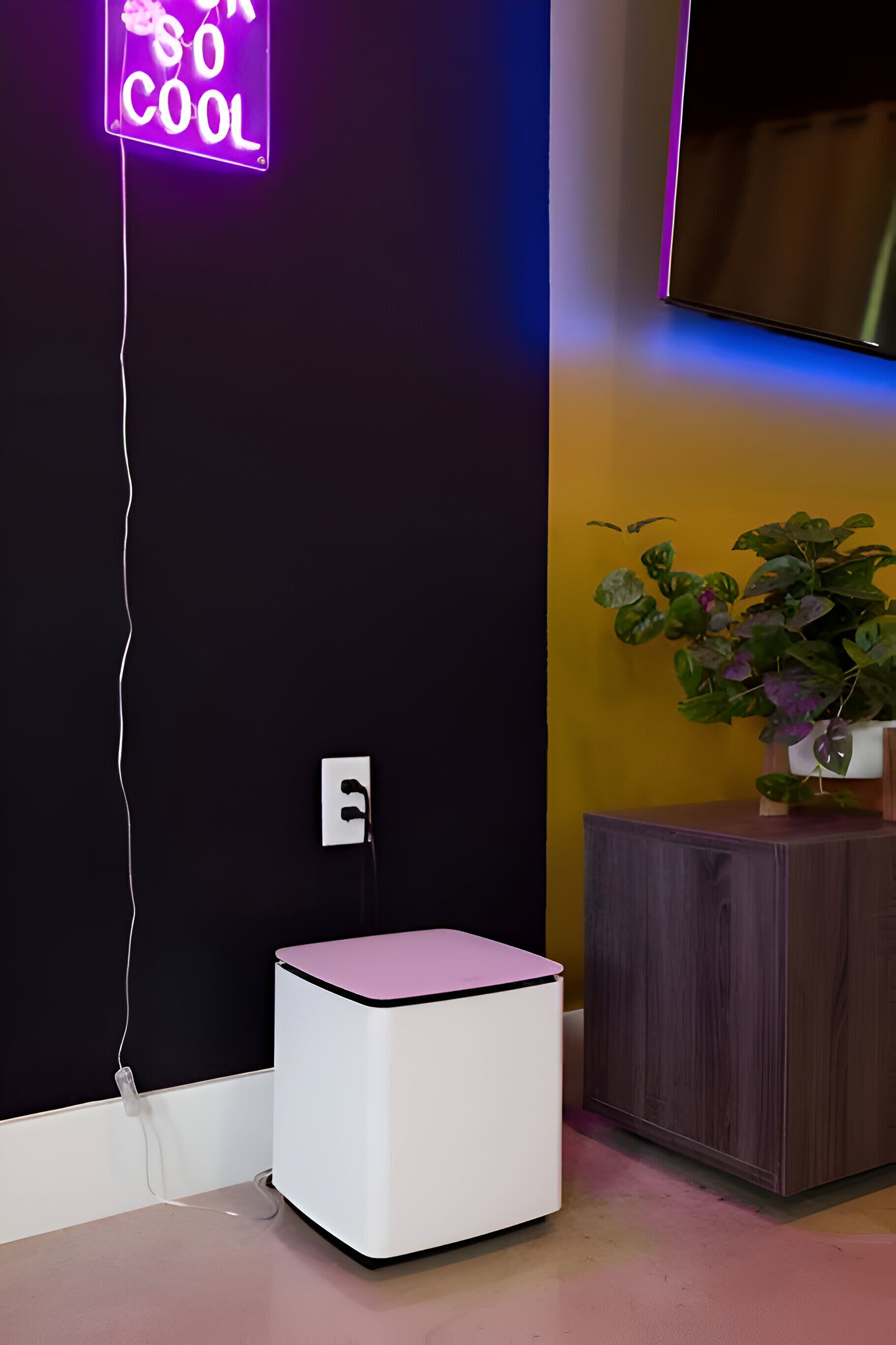A room with a neon sign, a small white table, a wooden cabinet, and a potted plant.