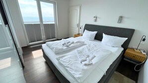 Une chambre à coucher avec un lit, une table de chevet, une lampe et une vue sur la mer par la fenêtre.