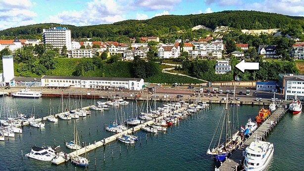 Un port de plaisance où sont amarrés de nombreux bateaux, entouré de bâtiments résidentiels et dominé, à l’arrière-plan, par un paysage vallonné.